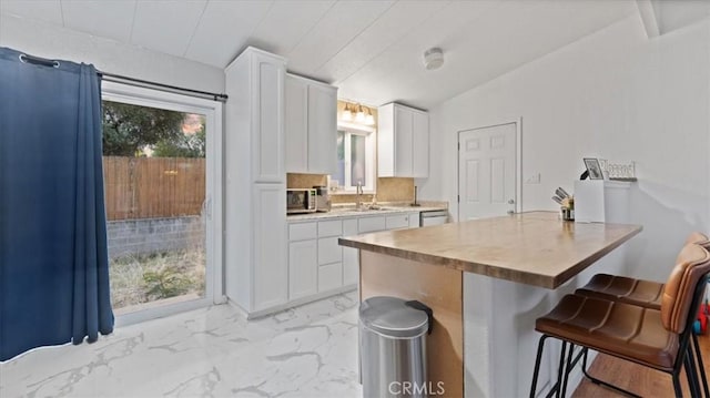 kitchen featuring white dishwasher, a kitchen breakfast bar, sink, vaulted ceiling, and white cabinetry