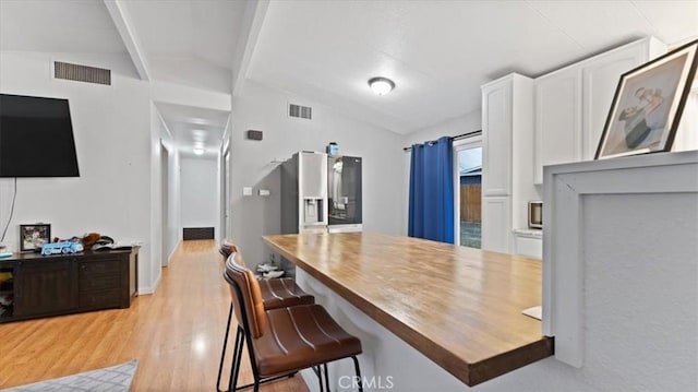 kitchen featuring a breakfast bar, butcher block counters, lofted ceiling, light wood-type flooring, and white cabinetry