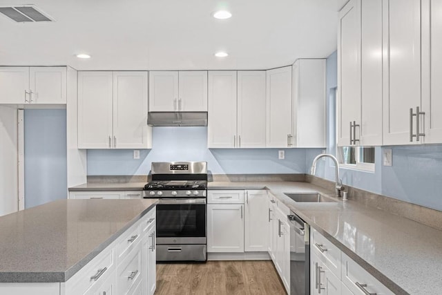 kitchen with stone counters, sink, white cabinetry, hardwood / wood-style flooring, and stainless steel appliances