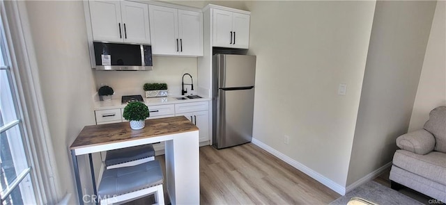 kitchen with wooden counters, appliances with stainless steel finishes, light wood-type flooring, sink, and white cabinetry