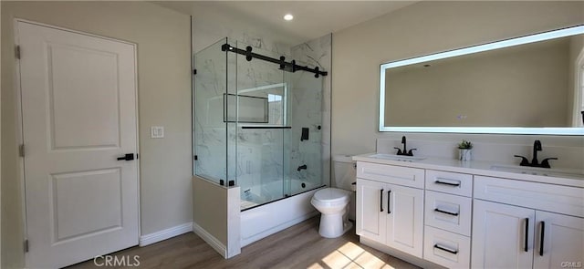 full bathroom with hardwood / wood-style floors, vanity, toilet, and bath / shower combo with glass door