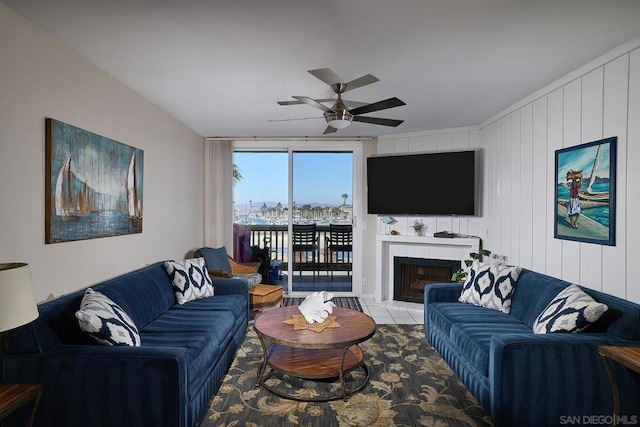 living room with a tiled fireplace, ceiling fan, and wooden walls