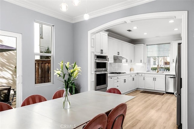 kitchen featuring white cabinets, sink, hanging light fixtures, light hardwood / wood-style flooring, and appliances with stainless steel finishes