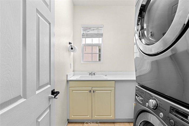 laundry area with cabinets, light tile patterned floors, stacked washer / dryer, and sink