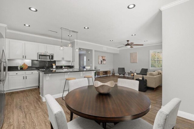 dining space featuring sink, wood-type flooring, ceiling fan, and crown molding