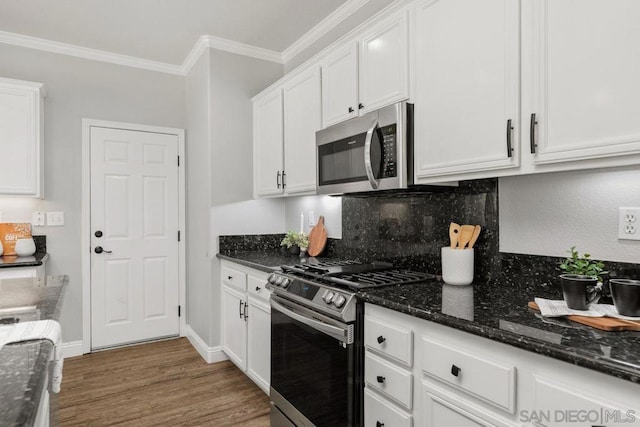 kitchen featuring crown molding, hardwood / wood-style flooring, white cabinetry, dark stone counters, and stainless steel appliances