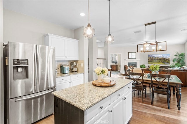 kitchen with white cabinetry, light hardwood / wood-style flooring, stainless steel fridge, pendant lighting, and a kitchen island