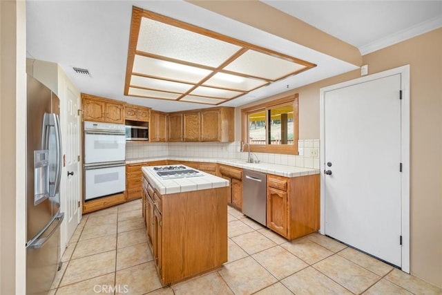 kitchen featuring decorative backsplash, appliances with stainless steel finishes, light tile patterned floors, tile countertops, and a kitchen island