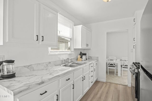 kitchen featuring light stone counters, sink, white cabinets, light hardwood / wood-style floors, and stainless steel range with gas cooktop