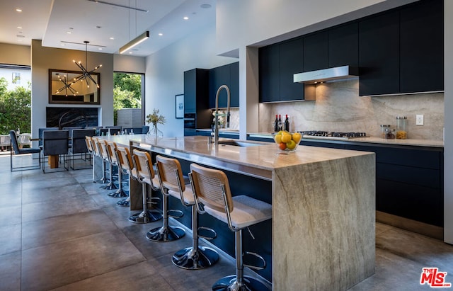 kitchen with backsplash, a spacious island, sink, decorative light fixtures, and a breakfast bar area