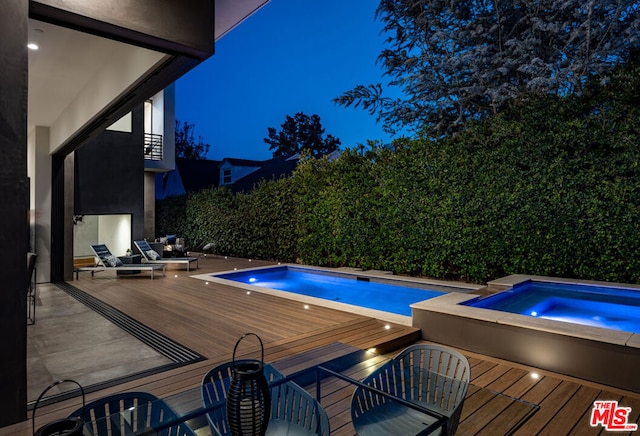 pool at twilight with an in ground hot tub and a wooden deck