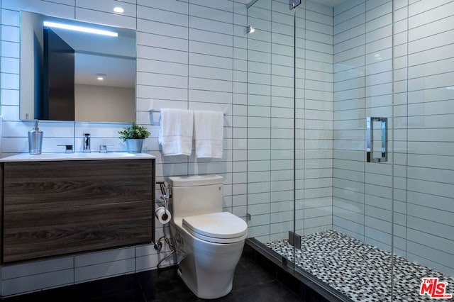 bathroom featuring vanity, a shower with door, tile patterned floors, toilet, and tile walls