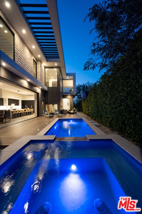 pool at twilight featuring an in ground hot tub and a deck