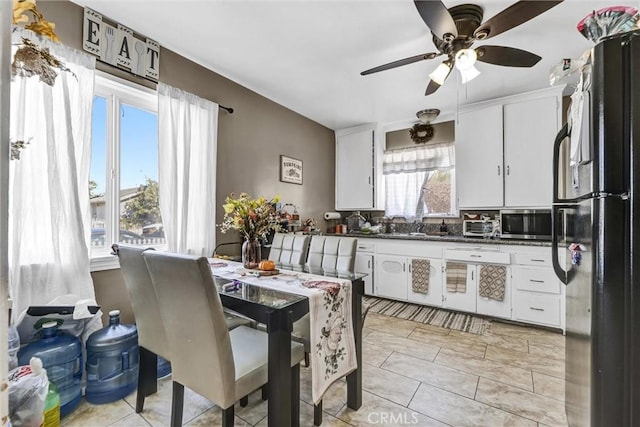 kitchen featuring ceiling fan, black refrigerator, white cabinetry, and light tile patterned floors