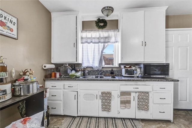 kitchen with sink, dark stone countertops, and white cabinetry