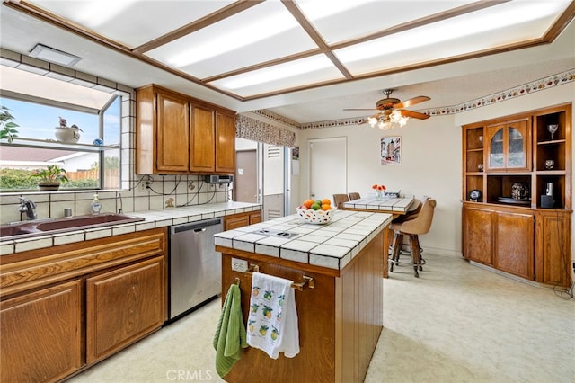 kitchen featuring sink, tile countertops, stainless steel dishwasher, a kitchen island, and decorative backsplash