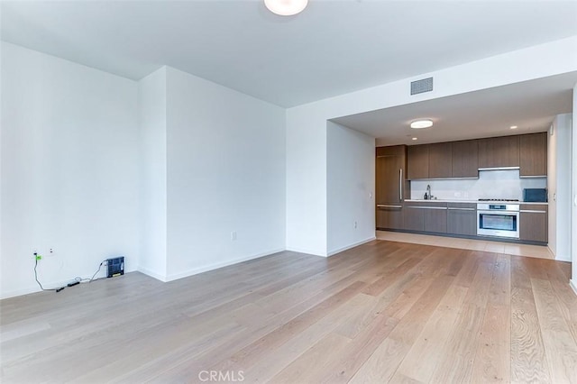 kitchen featuring oven, light hardwood / wood-style floors, cooktop, sink, and dark brown cabinetry