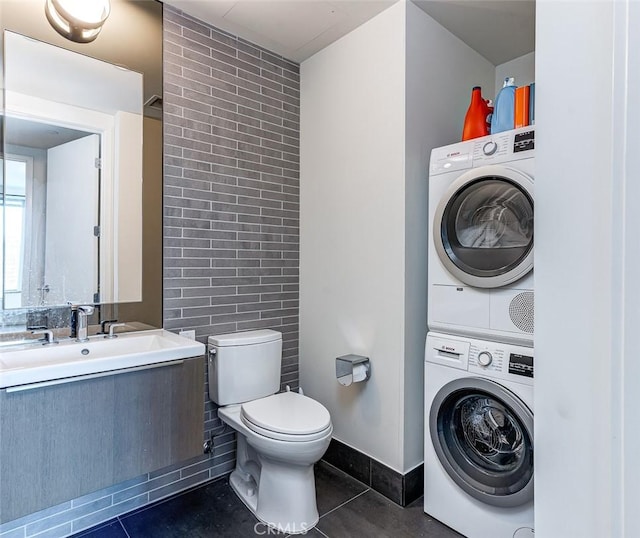 bathroom with toilet, stacked washer and dryer, and tile patterned flooring