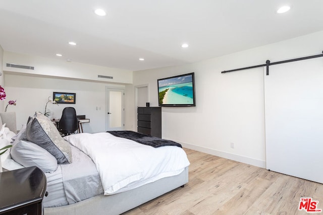 bedroom with a barn door and light hardwood / wood-style flooring