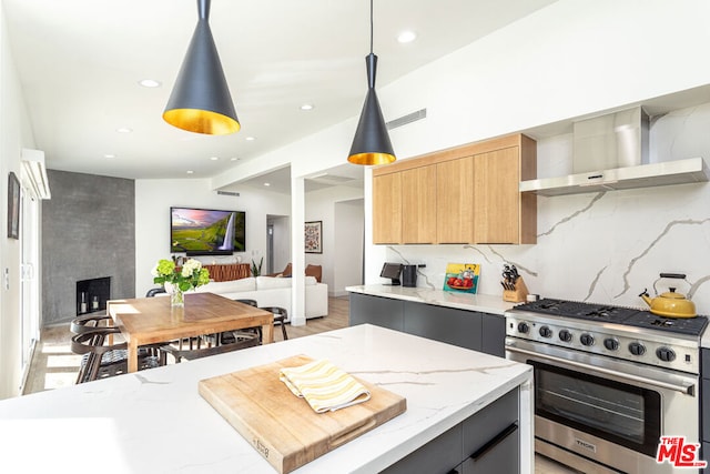 kitchen with a center island, wall chimney range hood, light stone counters, decorative light fixtures, and high end stainless steel range