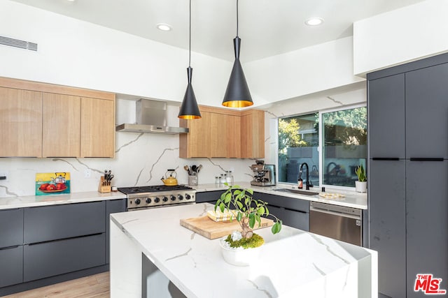 kitchen featuring appliances with stainless steel finishes, wall chimney exhaust hood, sink, decorative light fixtures, and a kitchen island