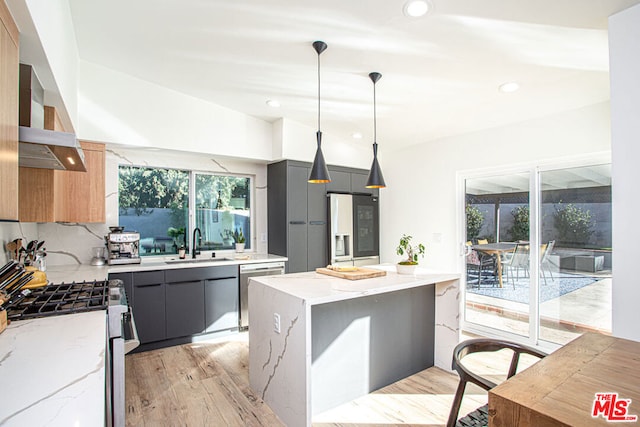 kitchen featuring light stone countertops, backsplash, stainless steel appliances, wall chimney range hood, and pendant lighting