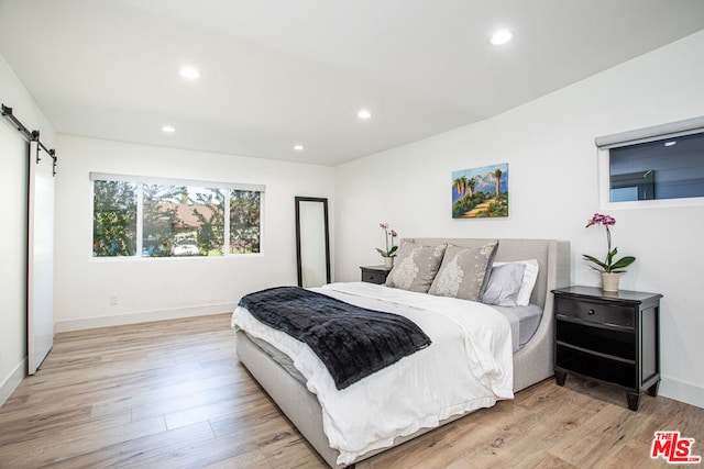 bedroom featuring a barn door and light hardwood / wood-style floors