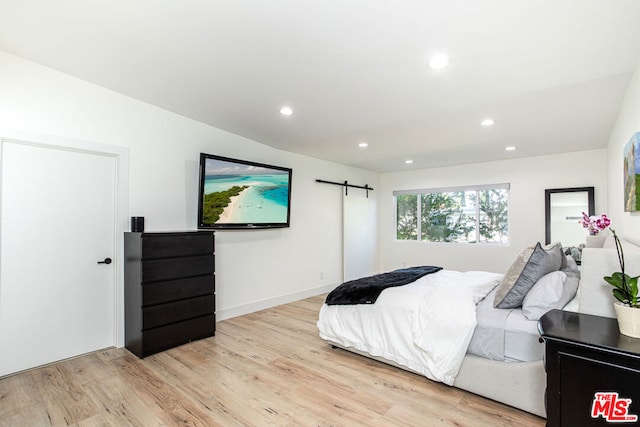 bedroom with a barn door and light wood-type flooring