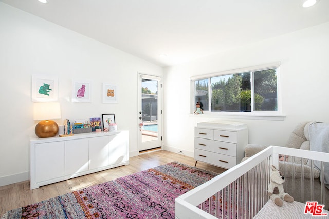 bedroom with vaulted ceiling, a crib, and light hardwood / wood-style flooring