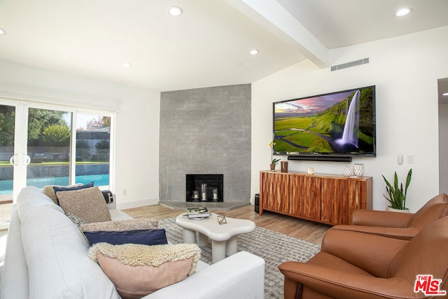 living room featuring vaulted ceiling with beams, light hardwood / wood-style floors, and a fireplace