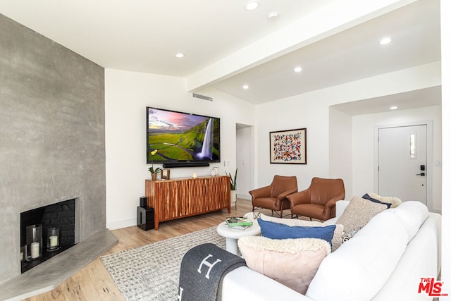 living room featuring a large fireplace, vaulted ceiling with beams, and light hardwood / wood-style flooring