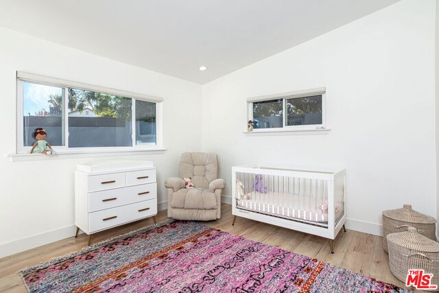 bedroom with lofted ceiling, a crib, and light wood-type flooring