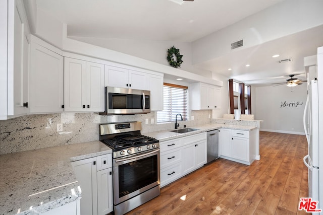 kitchen featuring kitchen peninsula, stainless steel appliances, vaulted ceiling, sink, and light hardwood / wood-style flooring