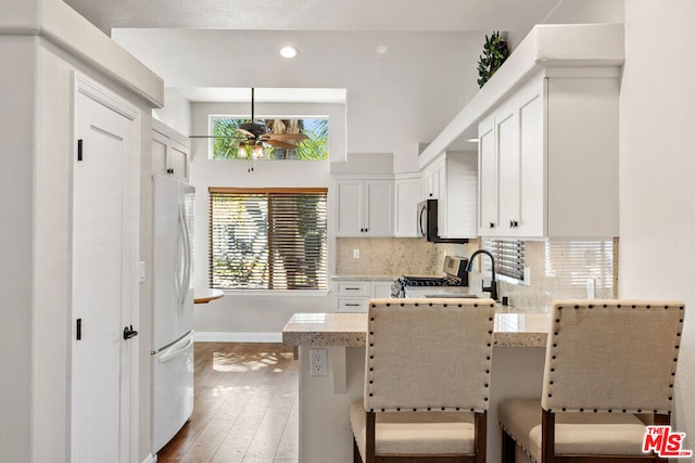 kitchen featuring a kitchen breakfast bar, sink, light stone counters, white cabinetry, and stainless steel appliances