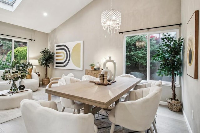 dining room featuring high vaulted ceiling, a chandelier, light wood-type flooring, and a skylight