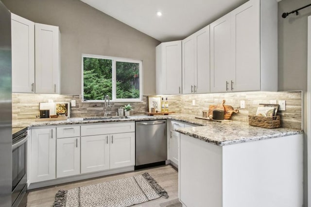 kitchen with appliances with stainless steel finishes, white cabinetry, lofted ceiling, sink, and light stone countertops