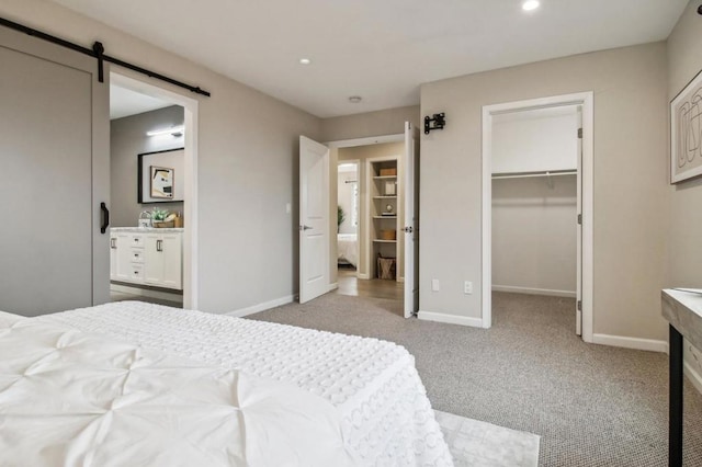 bedroom featuring connected bathroom, a walk in closet, a barn door, light carpet, and a closet