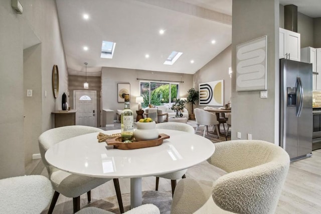 dining area with a skylight, high vaulted ceiling, and light wood-type flooring