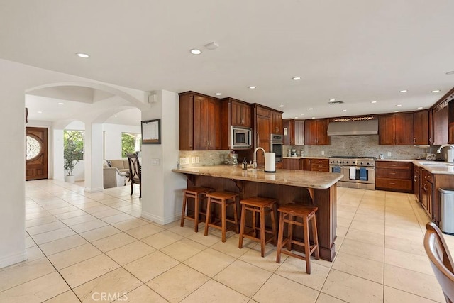 kitchen featuring light tile patterned floors, kitchen peninsula, appliances with stainless steel finishes, wall chimney exhaust hood, and sink