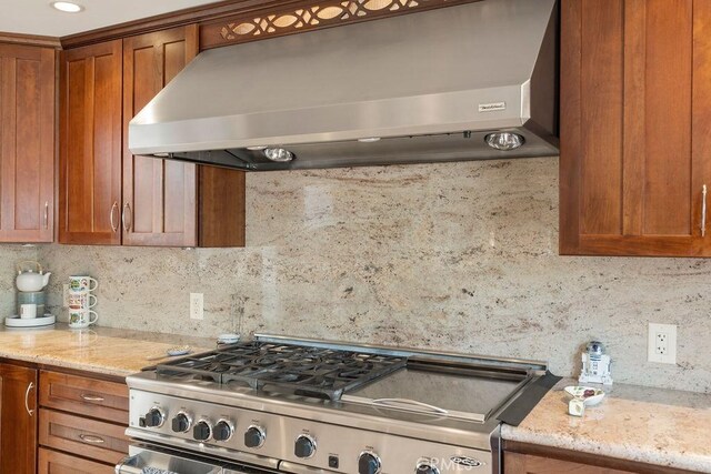 kitchen with stainless steel range oven, backsplash, light stone counters, and wall chimney range hood