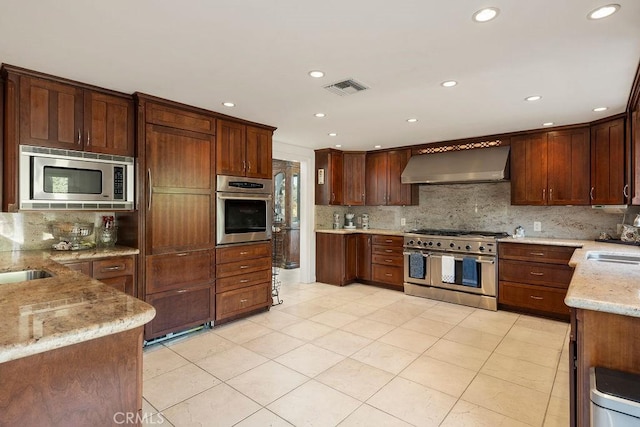 kitchen featuring wall chimney range hood, decorative backsplash, sink, light stone countertops, and appliances with stainless steel finishes