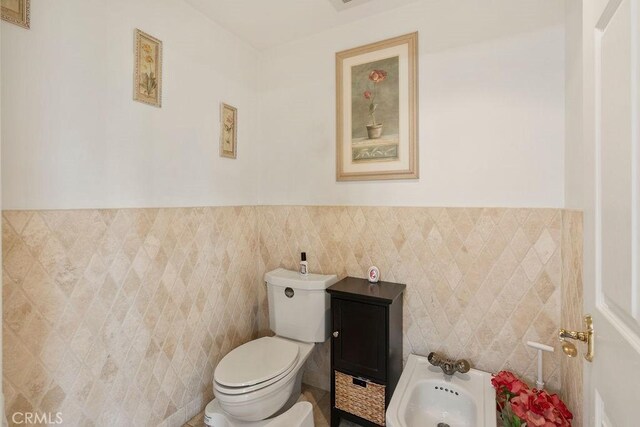 bathroom featuring a bidet, toilet, and tile walls