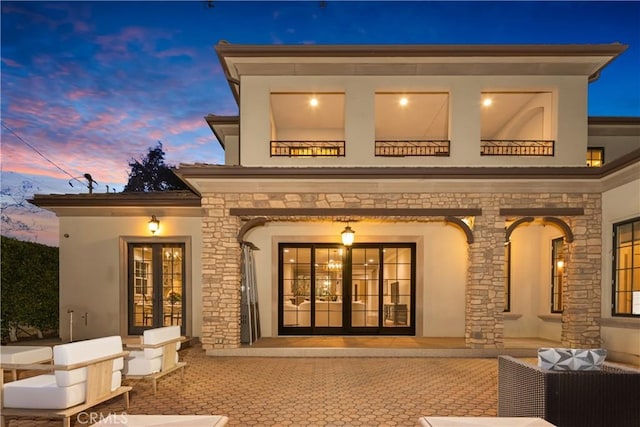 back house at dusk featuring outdoor lounge area, french doors, and a patio