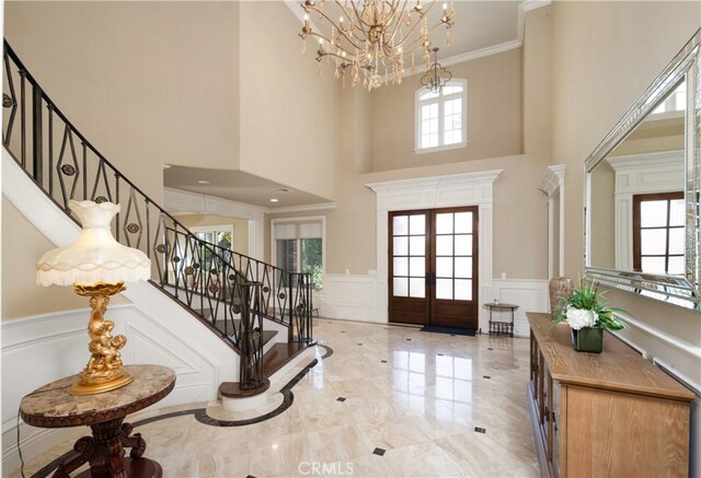 entryway featuring a towering ceiling, a notable chandelier, crown molding, and french doors