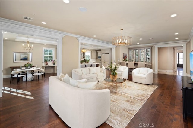 living room with dark wood-type flooring, ornamental molding, an inviting chandelier, and decorative columns