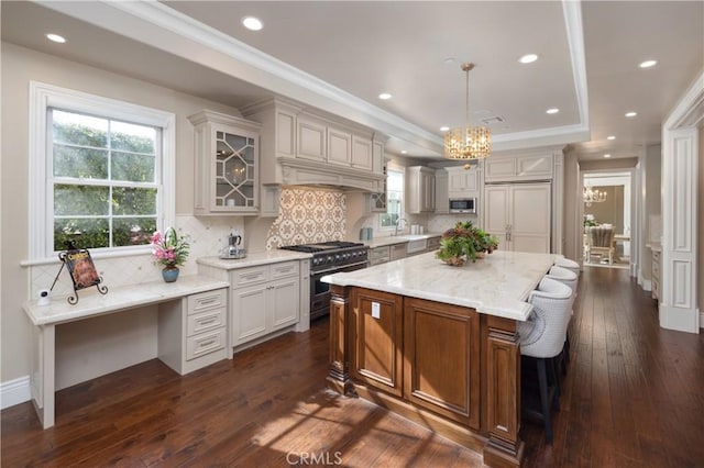 kitchen with a kitchen island, pendant lighting, a tray ceiling, light stone countertops, and high quality appliances