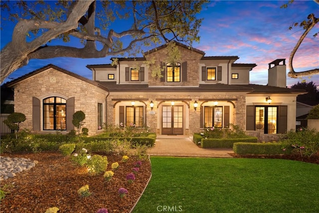 back house at dusk with french doors and a yard