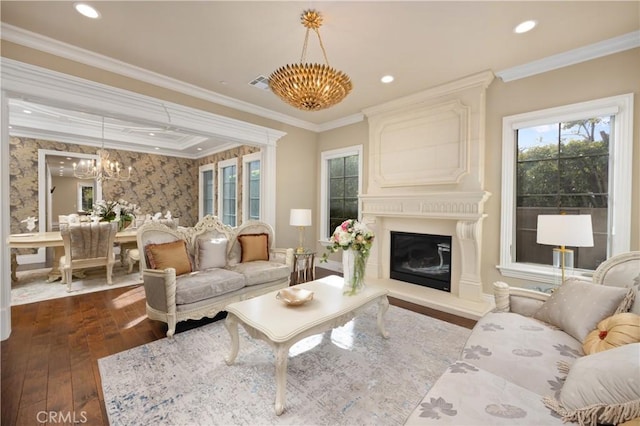 living room featuring dark wood-type flooring, a chandelier, a fireplace, and ornamental molding