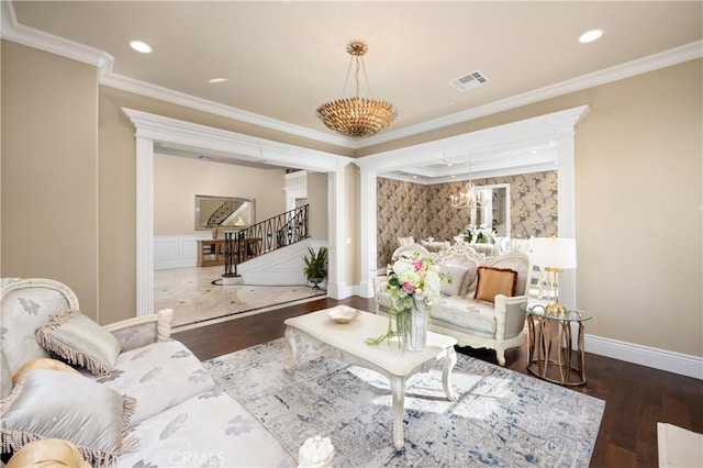 living room featuring decorative columns, dark hardwood / wood-style flooring, ornamental molding, and an inviting chandelier