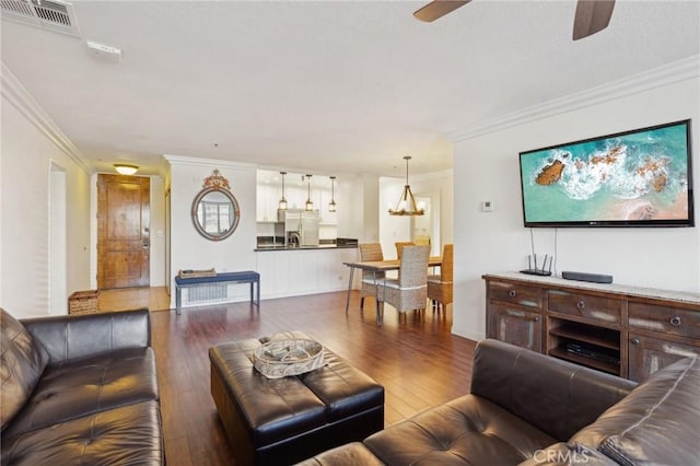 living room with dark hardwood / wood-style flooring, crown molding, and ceiling fan with notable chandelier